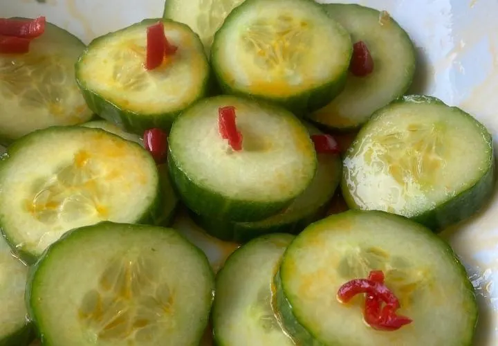 A bowl of Din Tai Fung style cucumber salad, sliced rounds in a garlic dressing with chilli oil on top