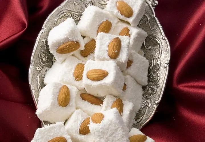 White Turkish delight cubes studded with whole almonds and dusted with sugar, on a silver plate