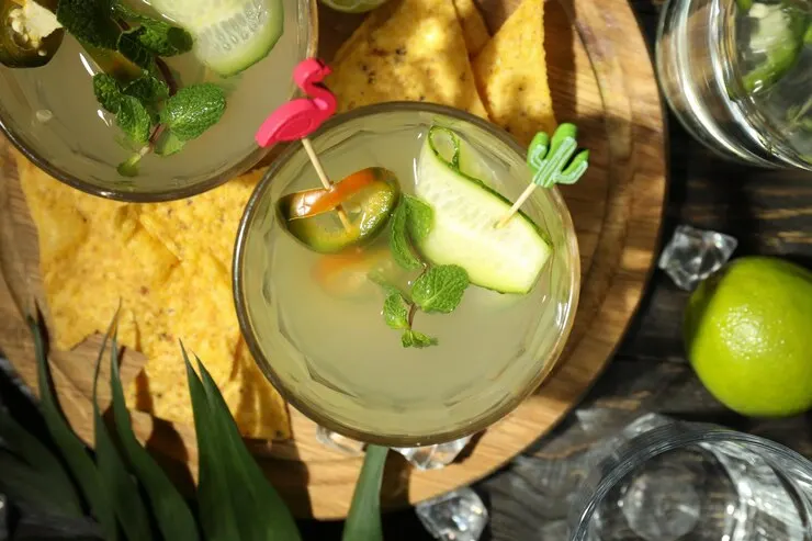 Two refreshing glasses of lemonade with cucumber and lime sit on a rustic wooden table, inviting a taste of summer.