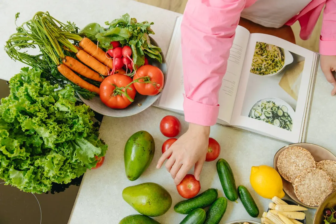 A woman is chopping fresh vegetables and arranging colourful fruits while preparing a healthy meal in her kitchen.