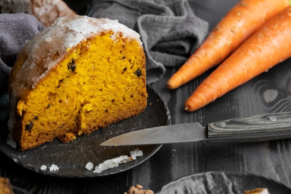 Vegan carrot cake topped with cream cheese frosting, elegantly presented on a white plate.